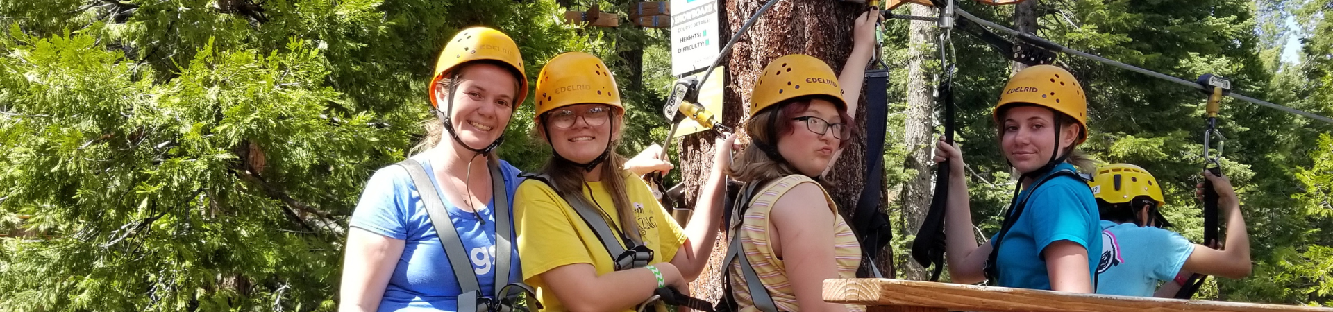  Girl Scouts wearing helmets on a high ropes course in the forest 